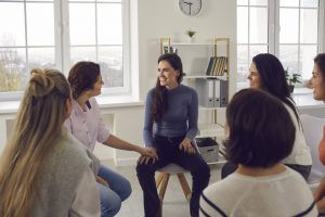 Happy women sitting in circle, smiling, talking and sharing positivity in group meeting